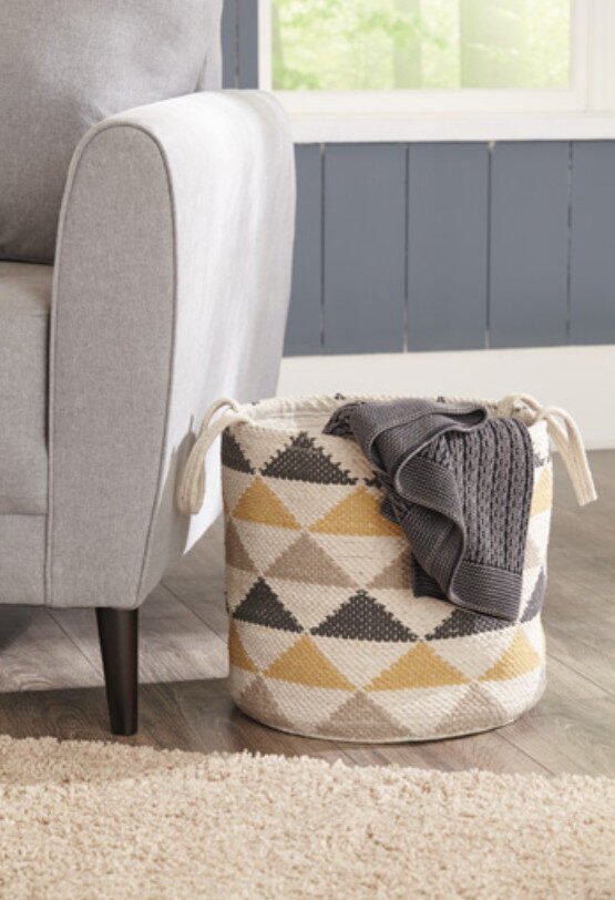 Geometric patterned storage basket with a grey throw blanket next to a light grey accent chair