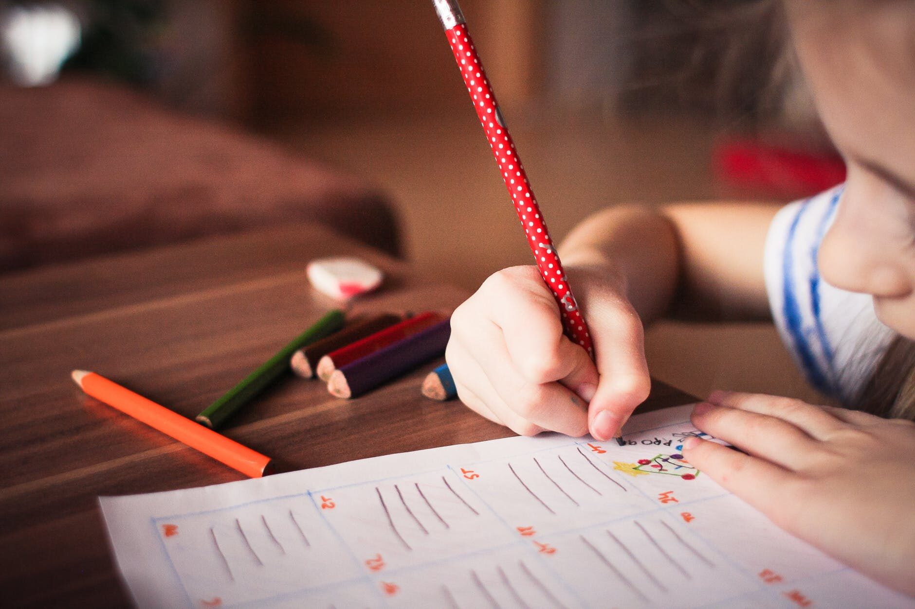 Child writing in a notebook with colorful pencils and eraser on the desk