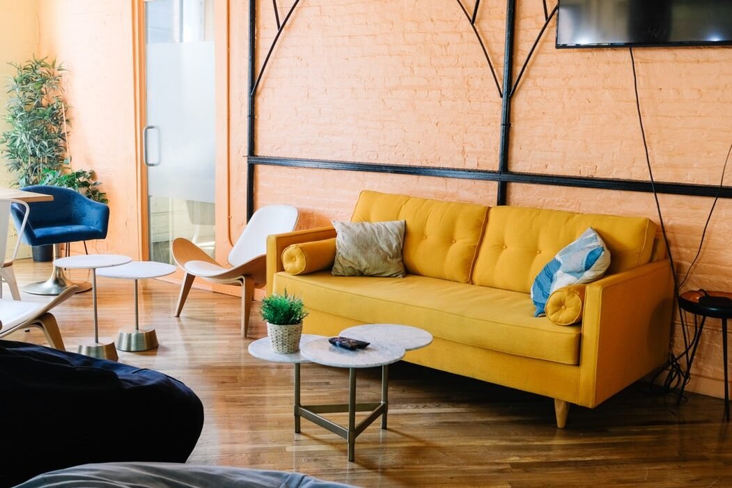 Modern living area with a yellow couch, wooden accent wall, and large industrial windows