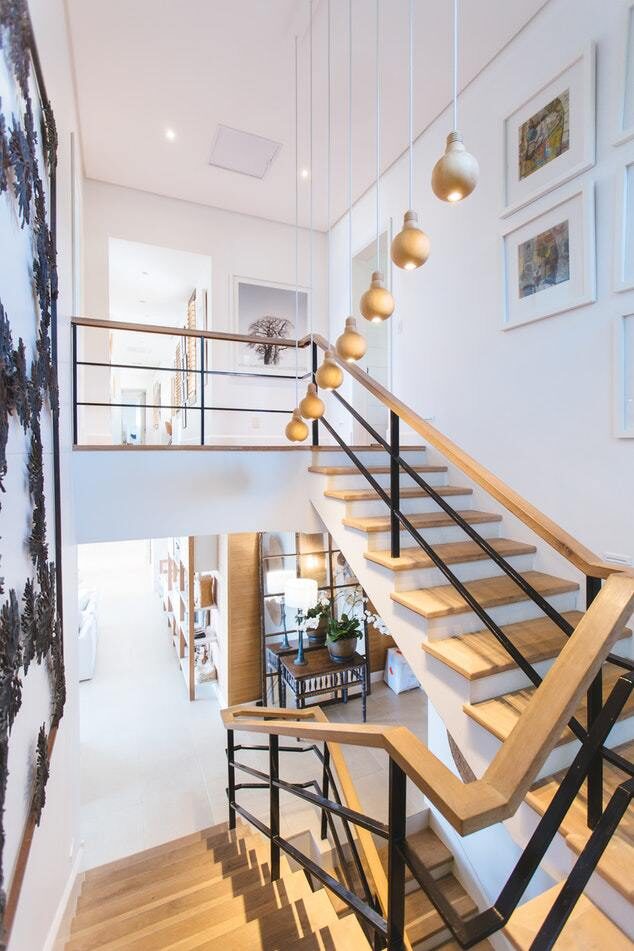 Modern staircase with wood steps, glass railings, and multiple gold pendant lights hanging from the high ceiling