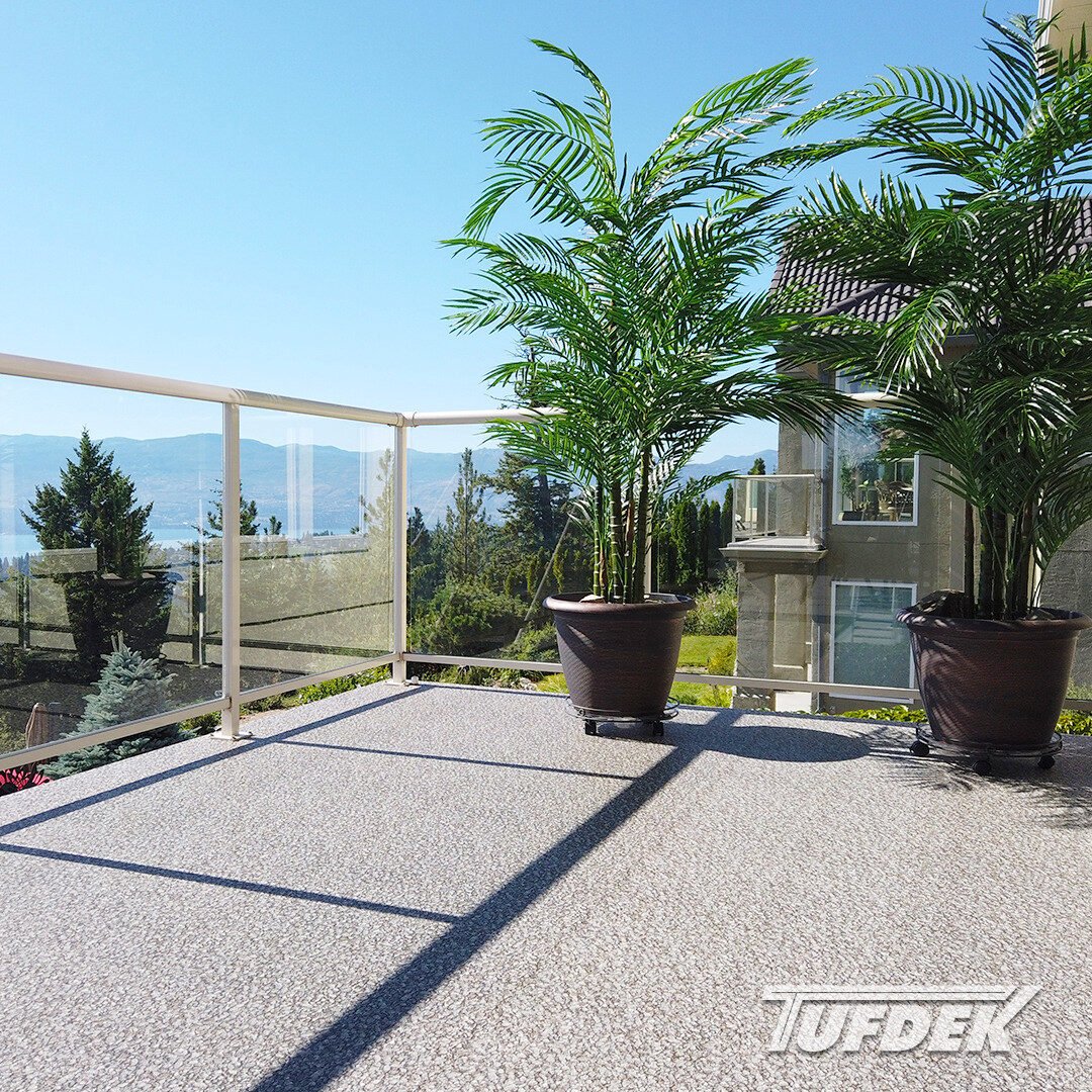 Outdoor balcony with weather-resistant flooring, potted palm plant, and glass railing overlooking scenic mountains and blue sky.